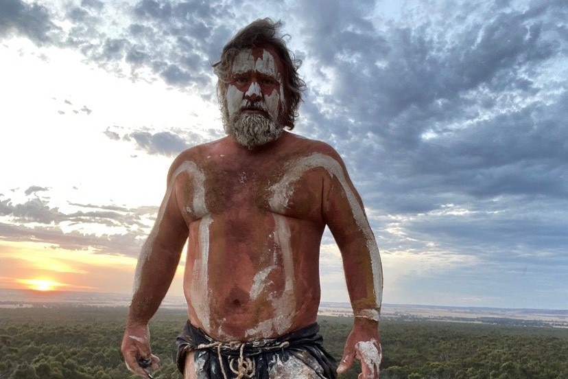 a man with body paint standing atop a hill with a setting sun in the background