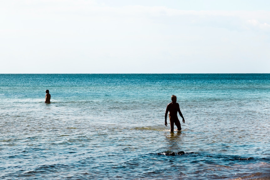 Two silhouetted swimmers in a blue sea.
