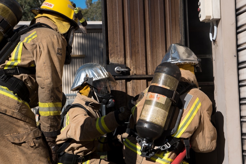 Three men from a team crouch and prepare to go into the fireroom.