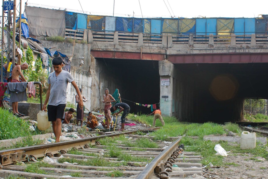 Residents have their morning wash and collect water from a pipe by a railway line