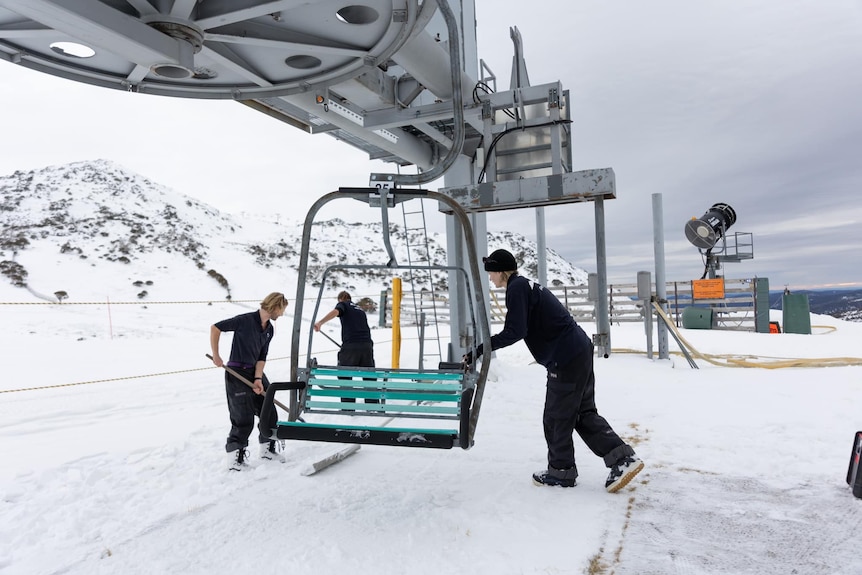 ski resort workers shovel away snow from ski lift