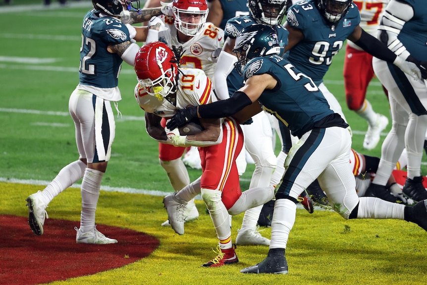 Eagles defenders try to wrap their arms around a Kansas City running back as he gets into the end zone for a touchdown.
