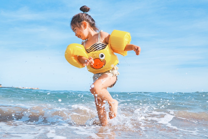 Young girl wearing flotation devices frolics at a beach