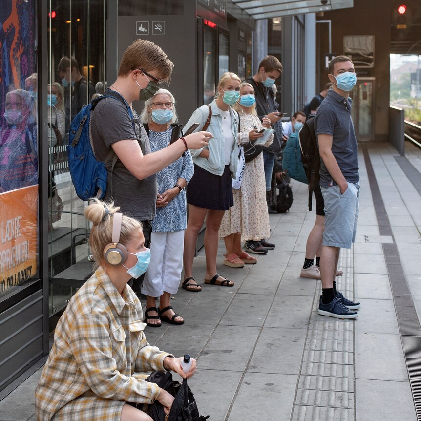 People wearing face masks stand on a train platform.