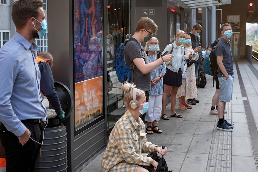 People wearing face masks stand on a train platform.