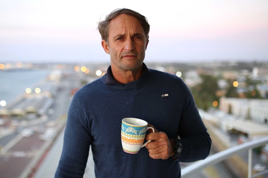 A man with a port in the background, holding a coffee cup.