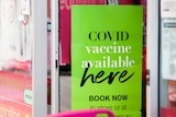 A sign outside a pharmacy reading 'COVID vaccine available here'.