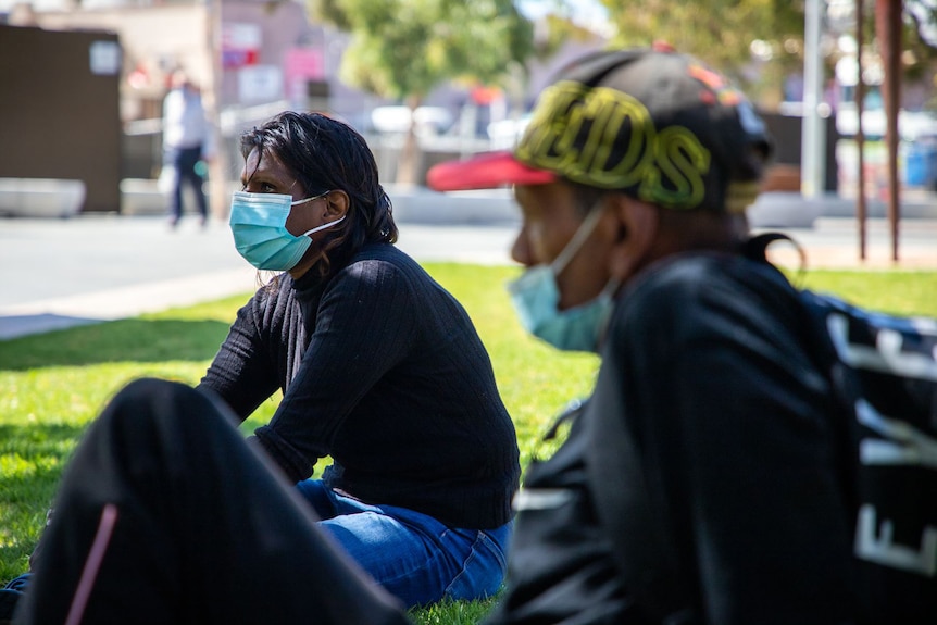 A couple sitting on grass wearing face masks