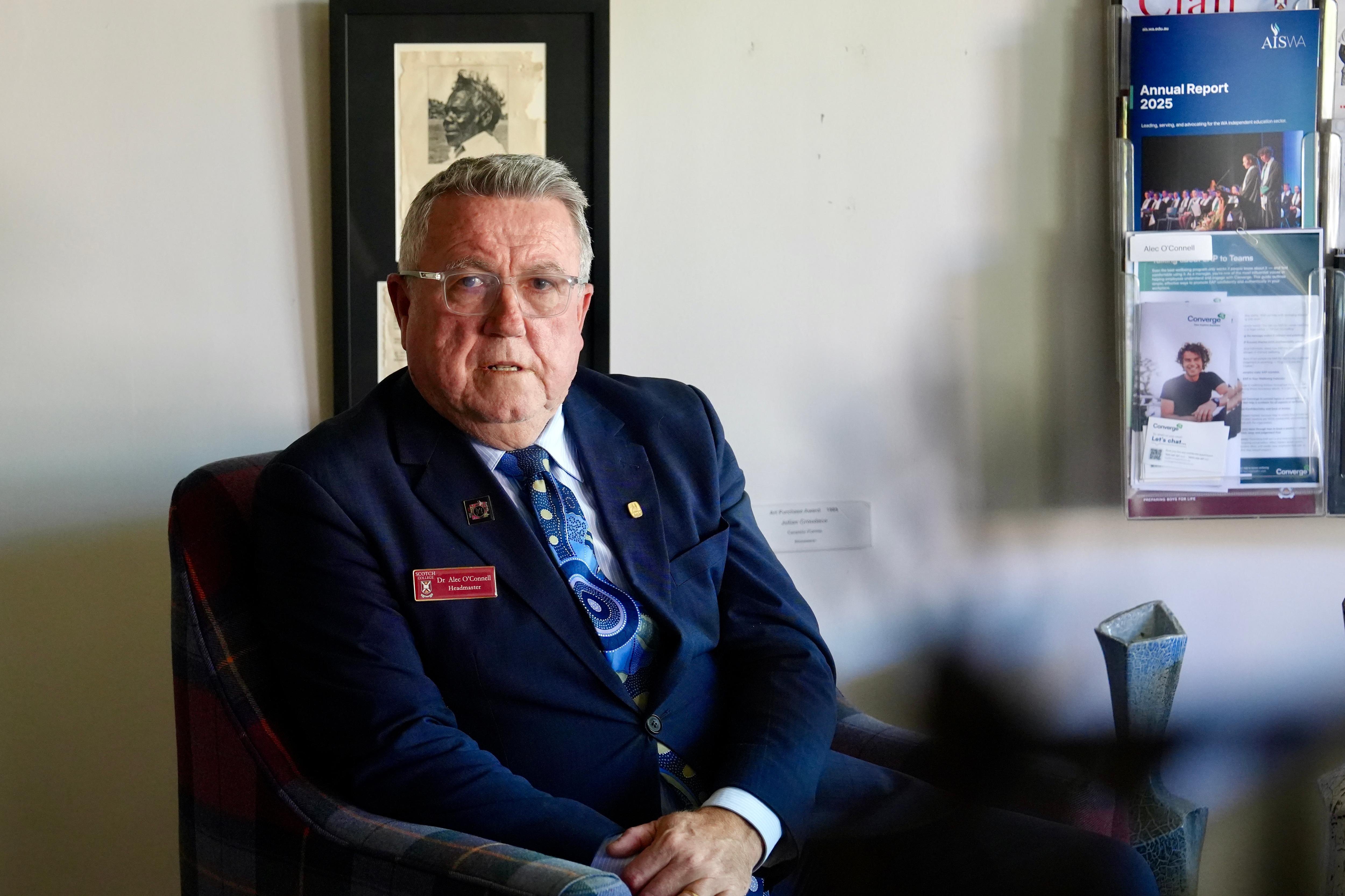 Alec O'Connell wears a blue blazer and tie as he sits in his office