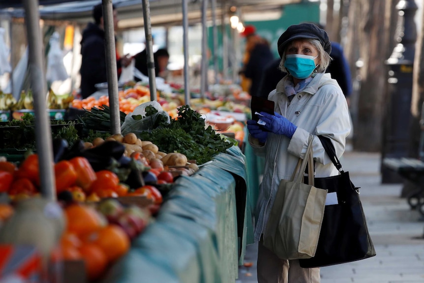A woman, wearing a protective face mask, shops for fruits and vegetables at the Bastille Market in Paris.