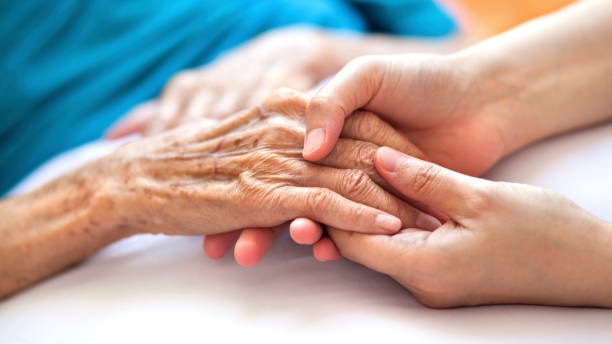 An elderly person holds hands with a younger person, only showing hands.