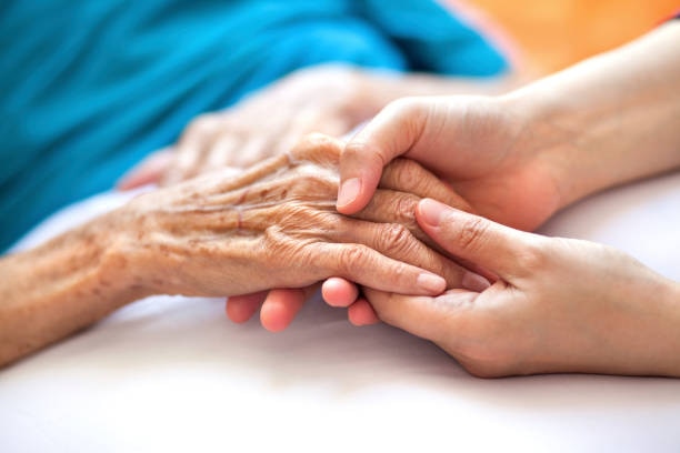 An elderly person holds hands with a younger person, only showing hands.