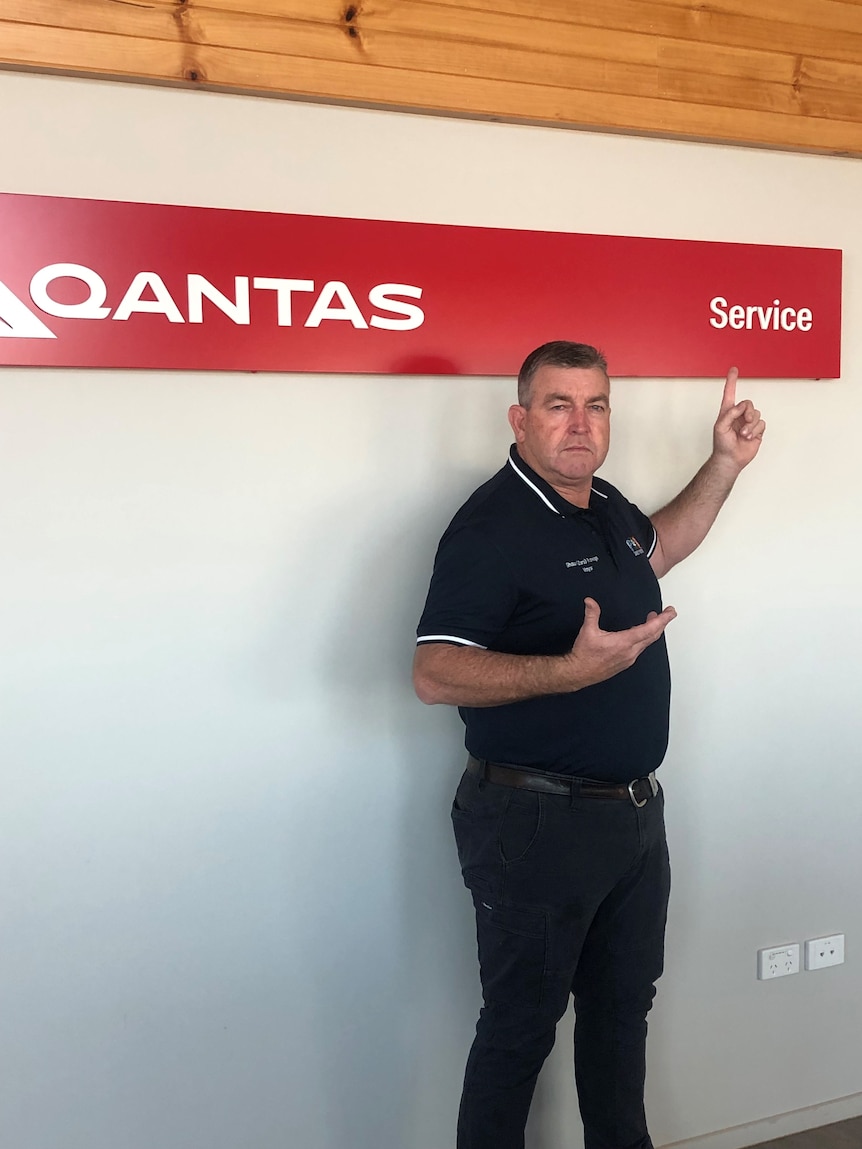 A man with a disappointed look on his face points at a sign that says "Qantas: Service".