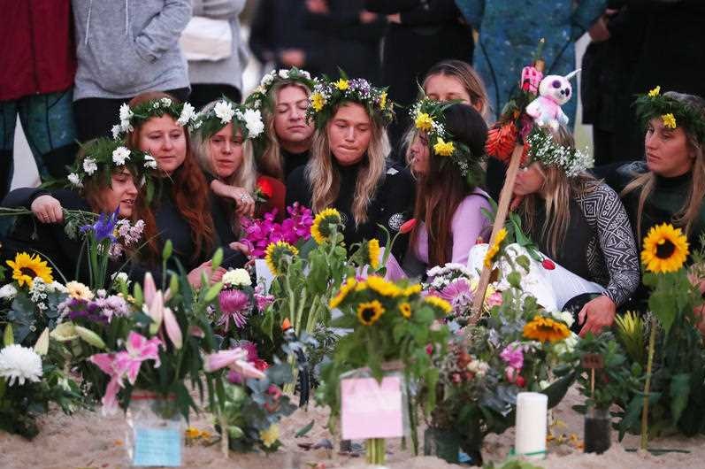 Women with flowers in their hair mourn on the beach.