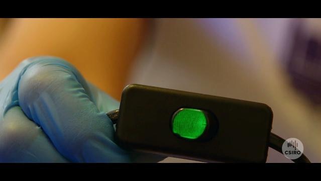 A gloved hand holds a small box with a glowing fingerprint on it
