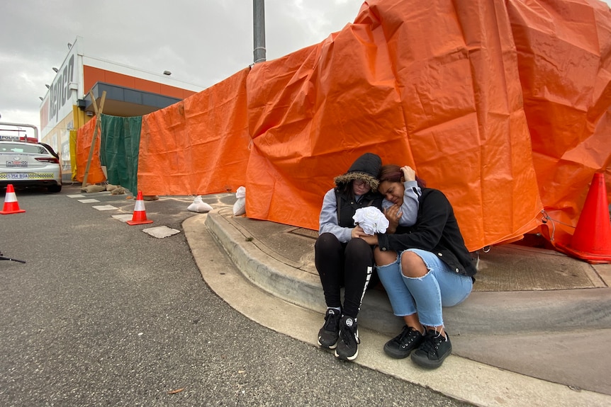 Two young girls embrace as they sit on a curb together