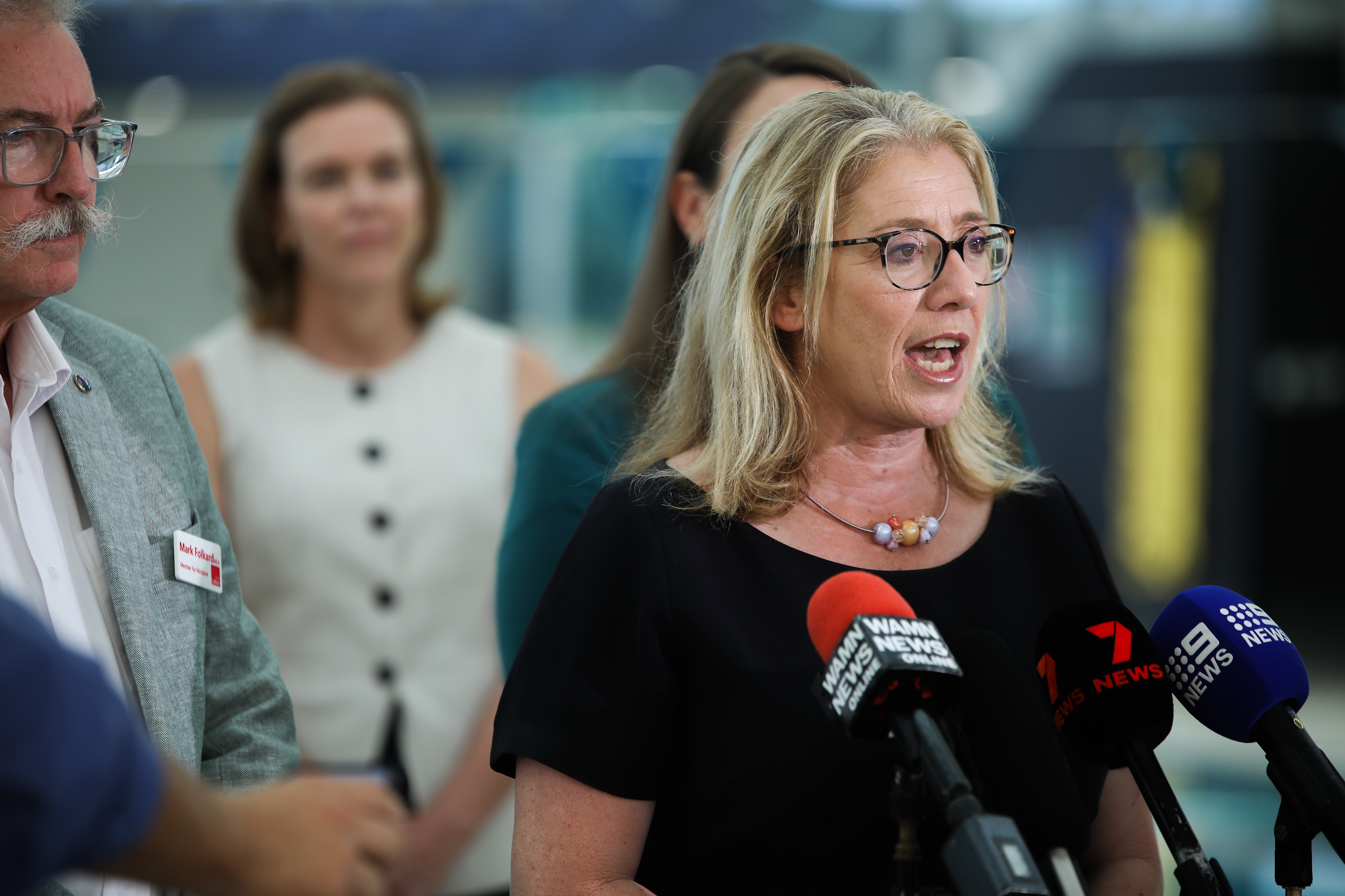 Женщина со светлыми волосами средней длины разговаривает с прессой 