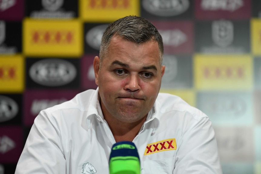 A dejected NRL coach sits with a microphone in front of him at a post-match press conference.