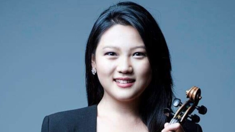 Emily Sun holding her violin in front of a blue background