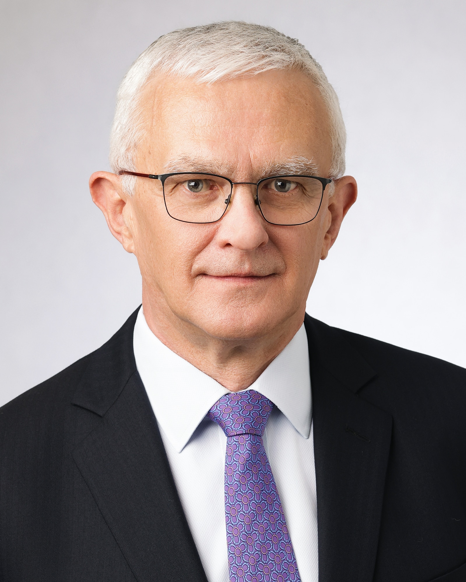 Un hombre con gafas y traje mira a la cámara.