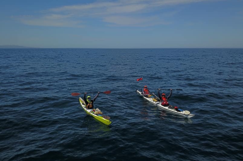 Three men in kayaks raise their arms in triumph