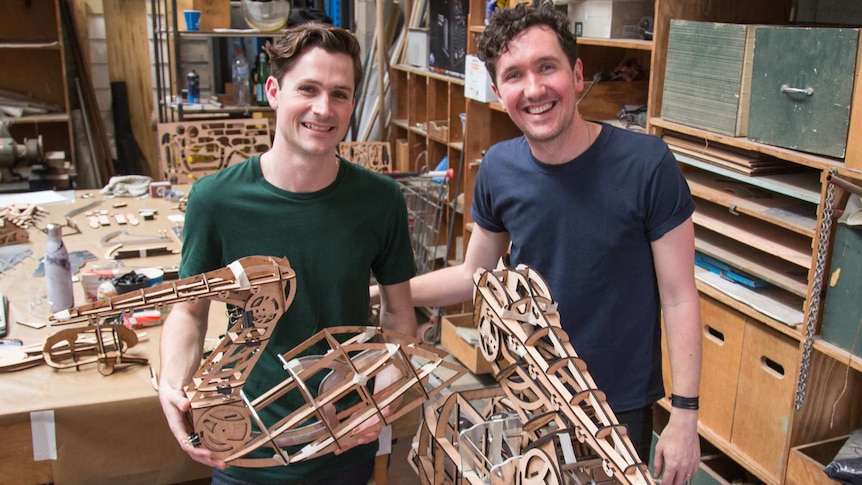 Two men holding pelican puppets made of wooden laser cuts.