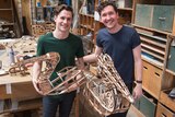 Two men holding pelican puppets made of wooden laser cuts.