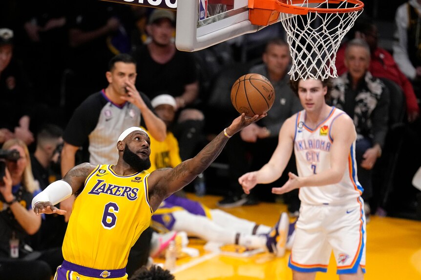 Basketballer LeBron James reaches out for a lay-up shot to the basket as defender Josh Giddey watches in the background.