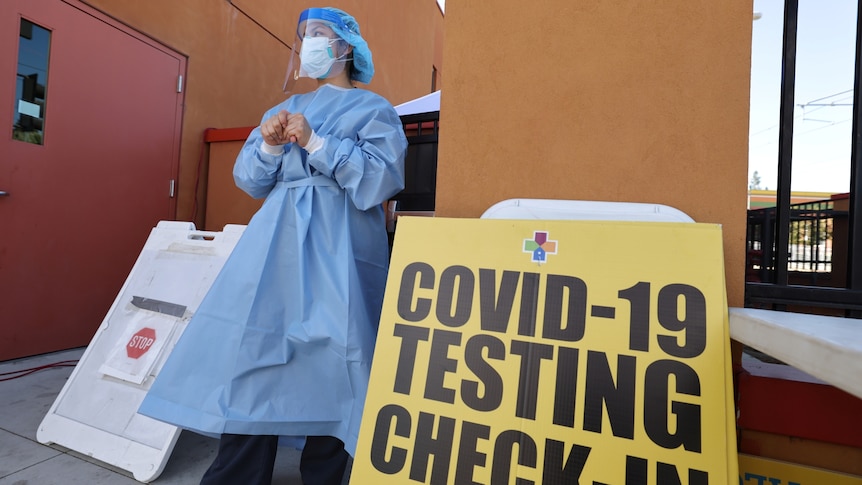 a nurse waits to test people for coronavirus next to a sign reading covid-19 testing check-in