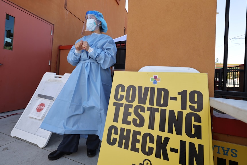a nurse waits to test people for coronavirus next to a sign reading covid-19 testing check-in