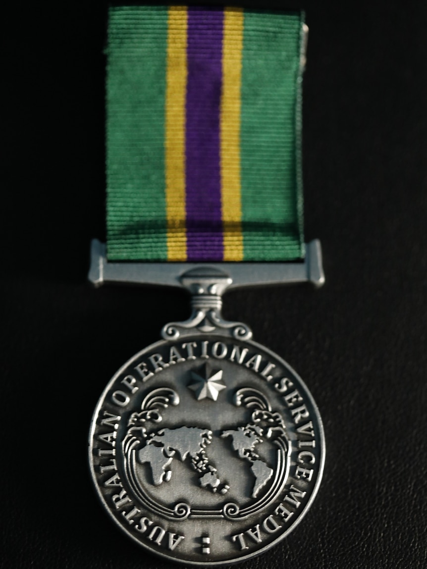 A silver Operational Service Medal with green, purple and yellow ribbon sits in a black box