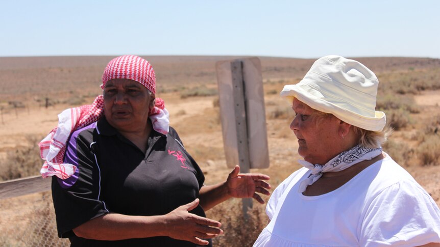 Two Aboriginal women stand in the dry landscape