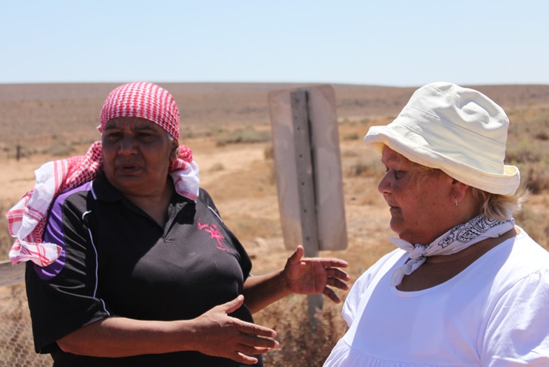 Two Aboriginal women stand in the dry landscape