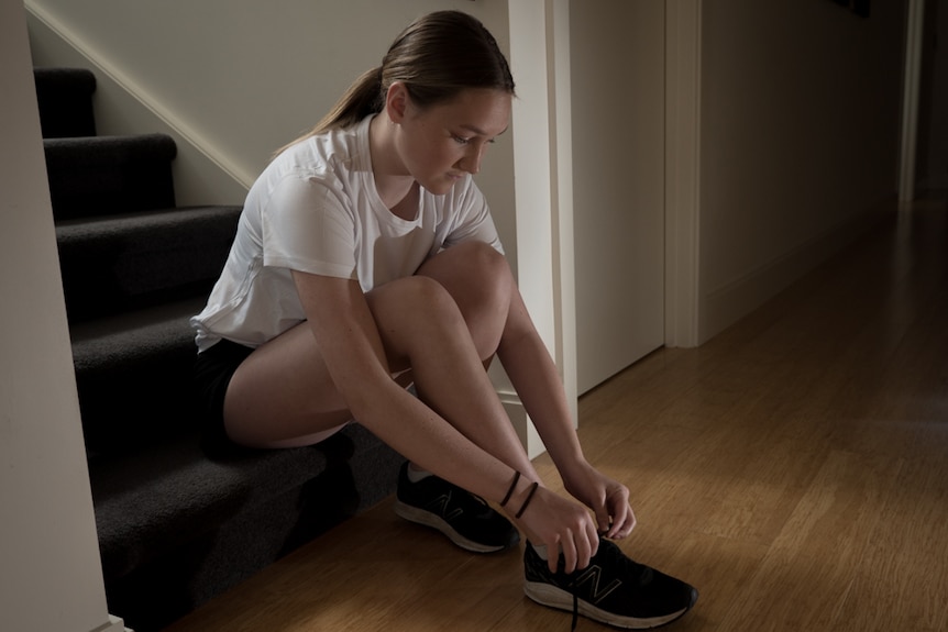 Mae Johnson sits on the stairs and ties her shoe laces.