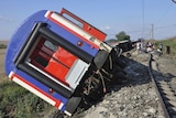 Blue train sits on its side with passengers sitting on the tracks