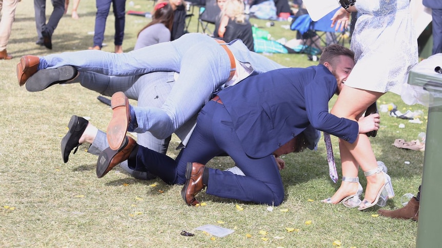 Three men are on their hands and knees with one clutching a standing woman for support