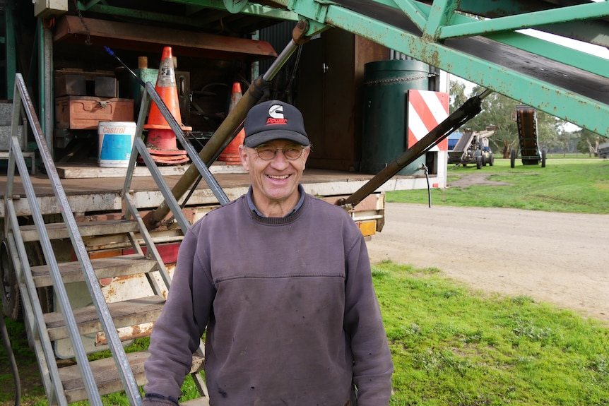 A farmer stands in front of a harvester.