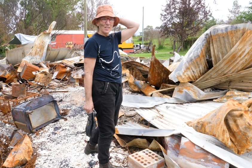 Veronica Cohen standing in the ruins of a burnt-down house holding gloves