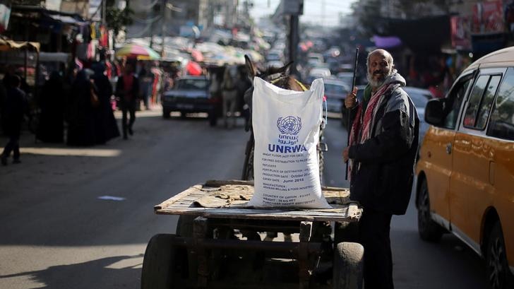 Man stands on the road next to flour sack with UNRWA logo on it sitting on a cart