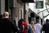 A line of people photographed from behind in front of a sign that reads Centrelink.