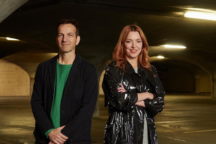 A man and a woman pose for a photo in a dimly-lit underground car park.