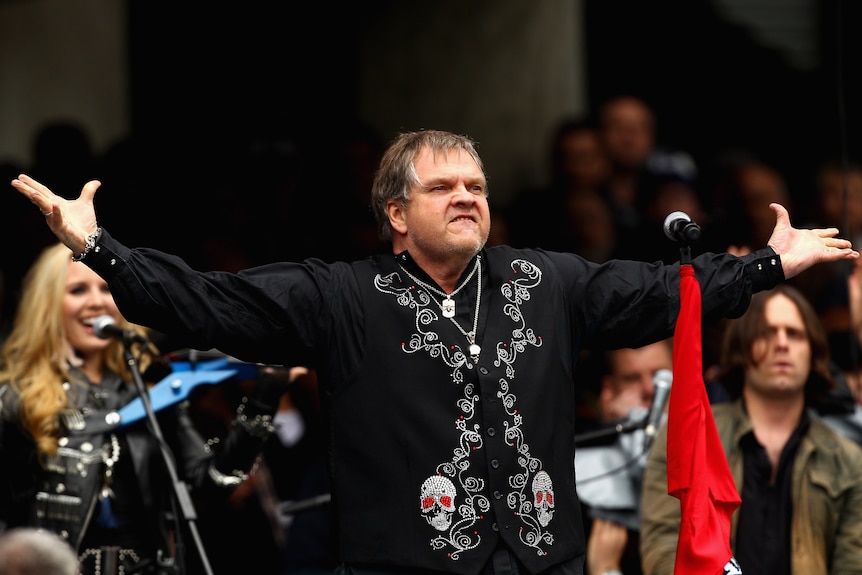 Musician stands with his arms extended to the crowd during an outdoor show.