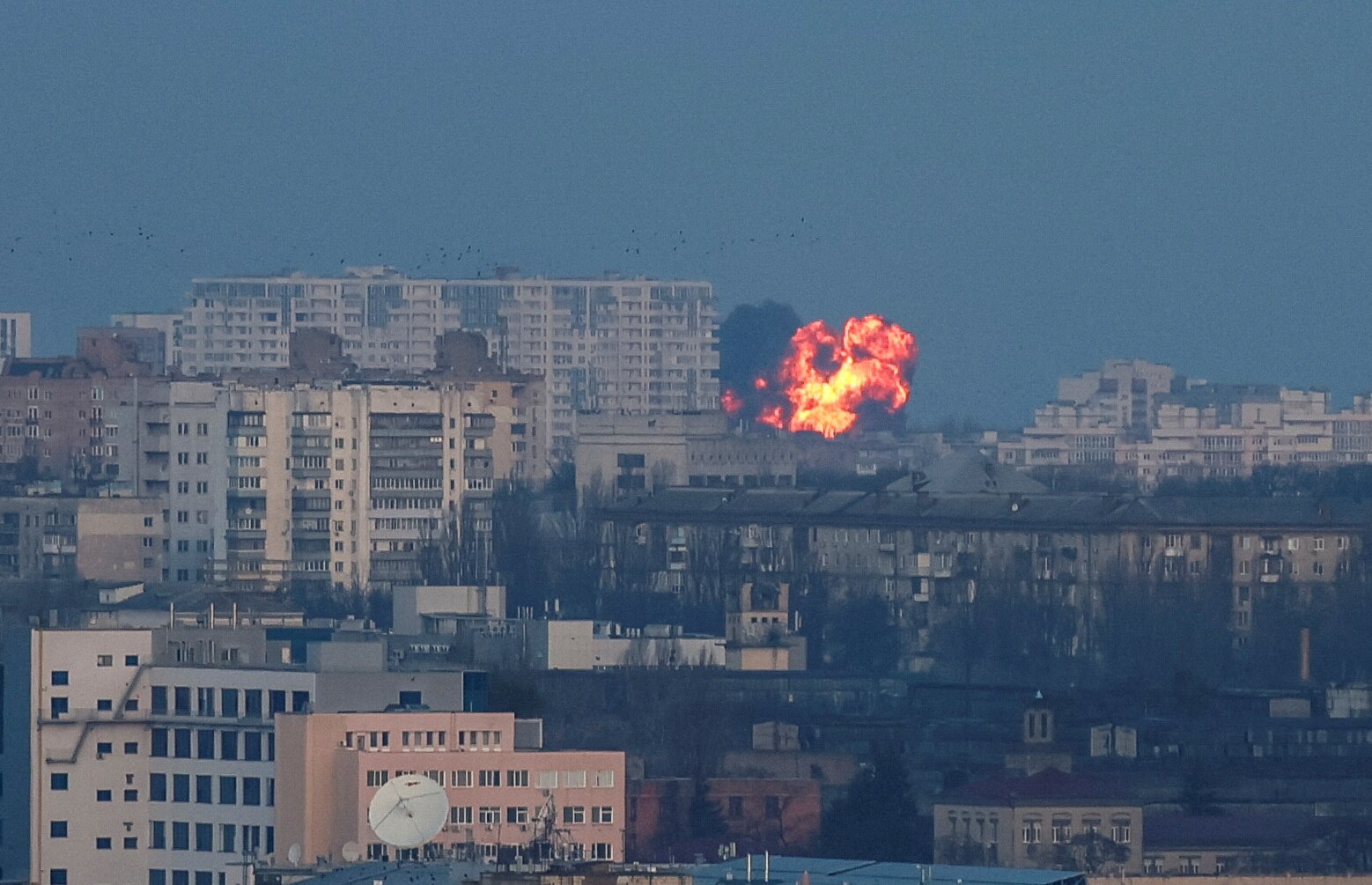 A wide aeiral photo of a skyling showing many apartment buildings and a ball of fire and smoke erupting in the background.