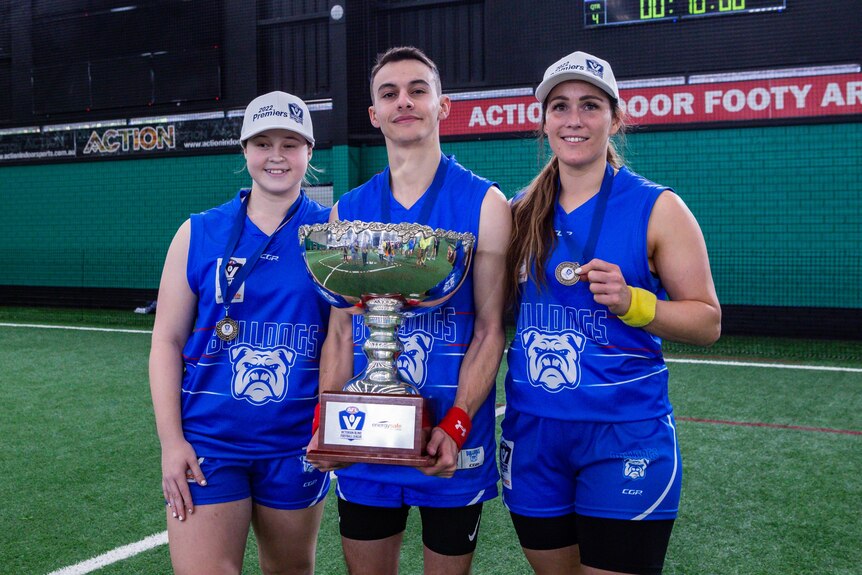 Three Bulldogs players pose with a large trophy.