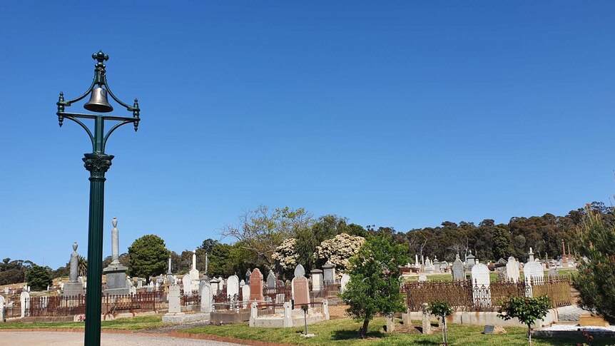 A cast iron bell atop a column among a row of graves.
