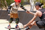 A little boy with a red helmte holds the hand of a man with a black cap at the top of a skate ramp