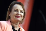 Sussan Ley smiles against a red and black backdrop.