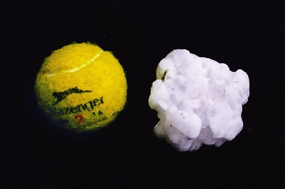 A yellow slazenger tennis ball sits next to a white hailstone that is larger in size. 