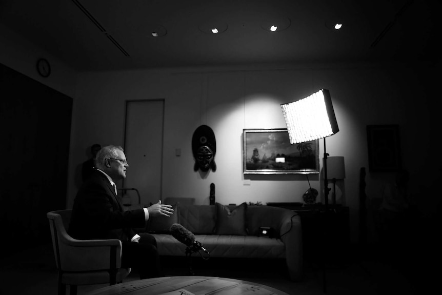 Black and white side shot of the prime minister sitting in chair looking towards camera and  large TV light.