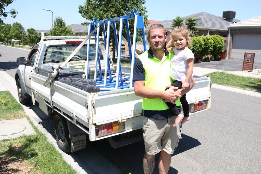 Jack Gray holds his daughter Scarlett in front of a ute.